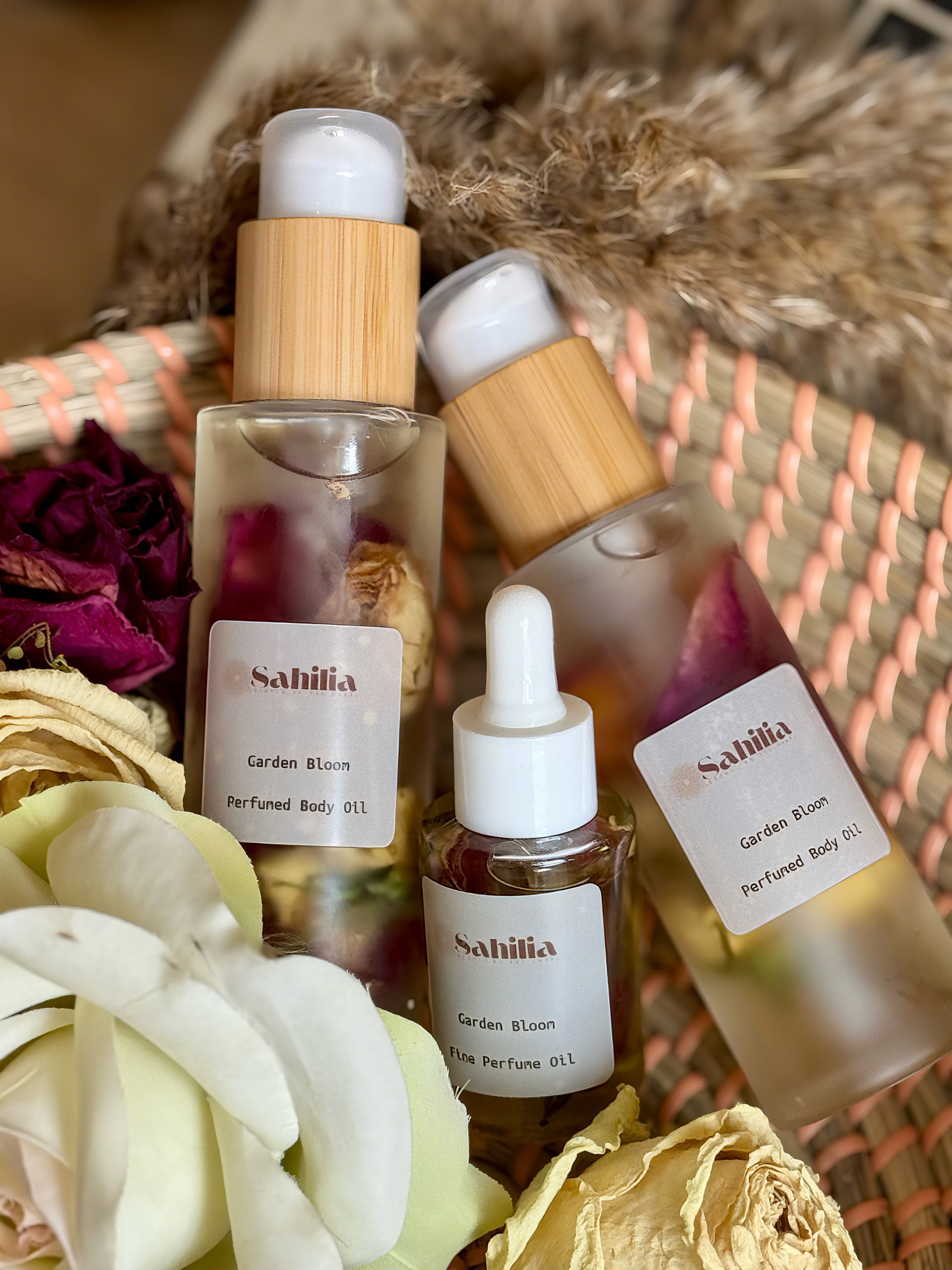 Collection of Sahilia Garden Bloom perfume oils with dried flowers and a woven basket in the background.