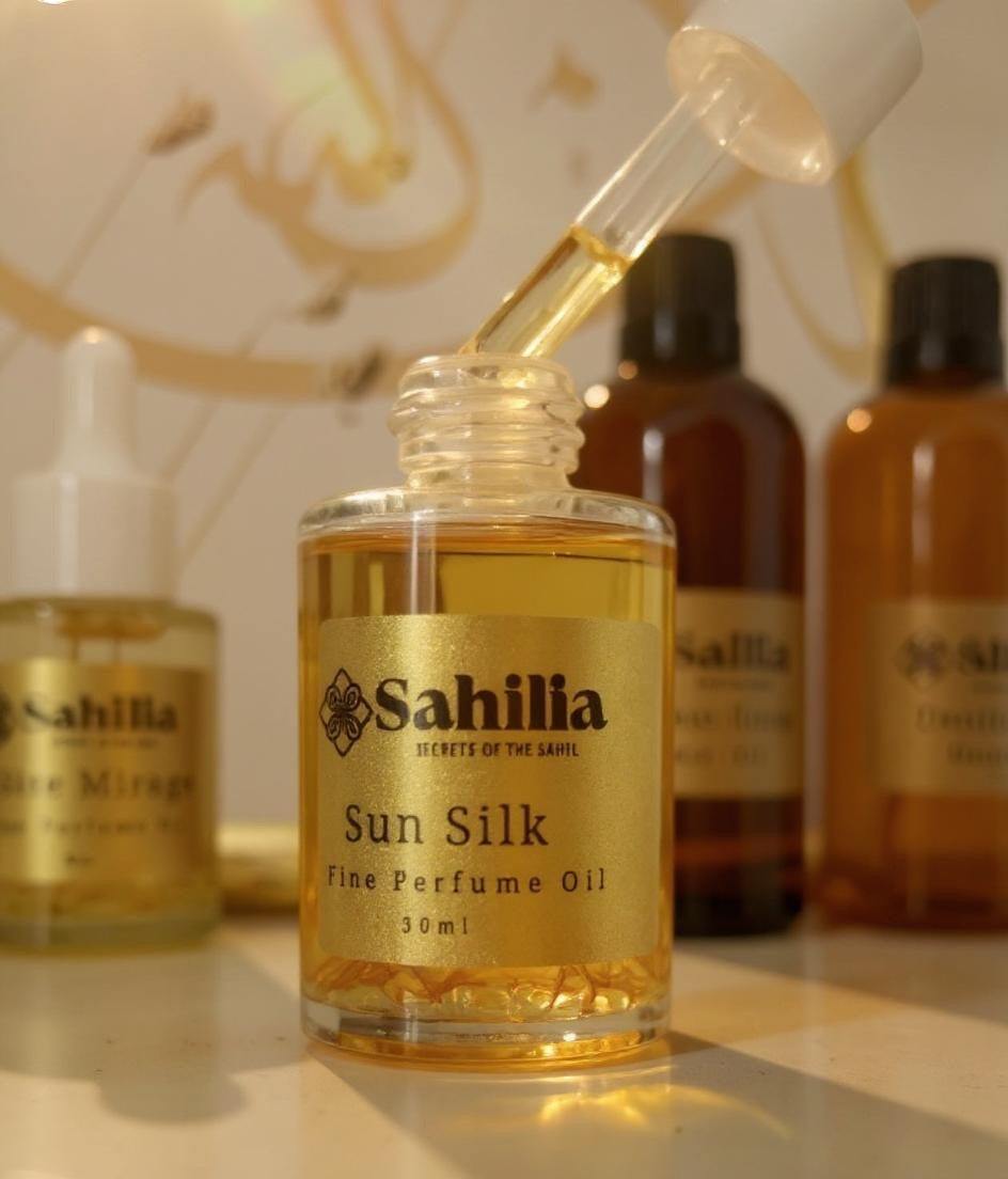 An open dropper perfume bottle with other perfume bottles and blurred out Arabic calligraphy in the background